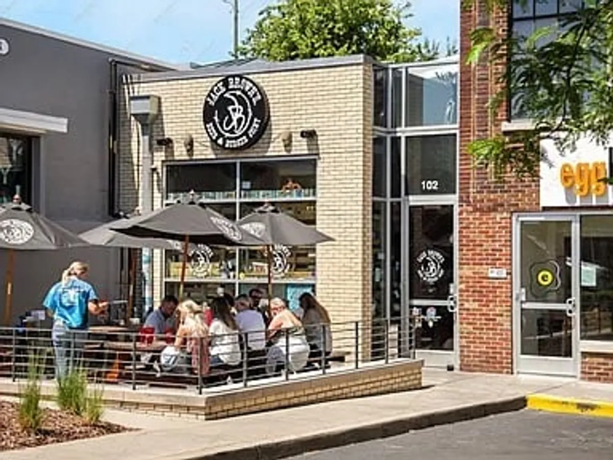 A lively exterior of a local restaurant featuring outdoor seating, vibrant signage, and customers enjoying meals under sunny skies. The setting is bustling yet relaxed, highlighting the social and culinary scene of the surrounding neighborhood.