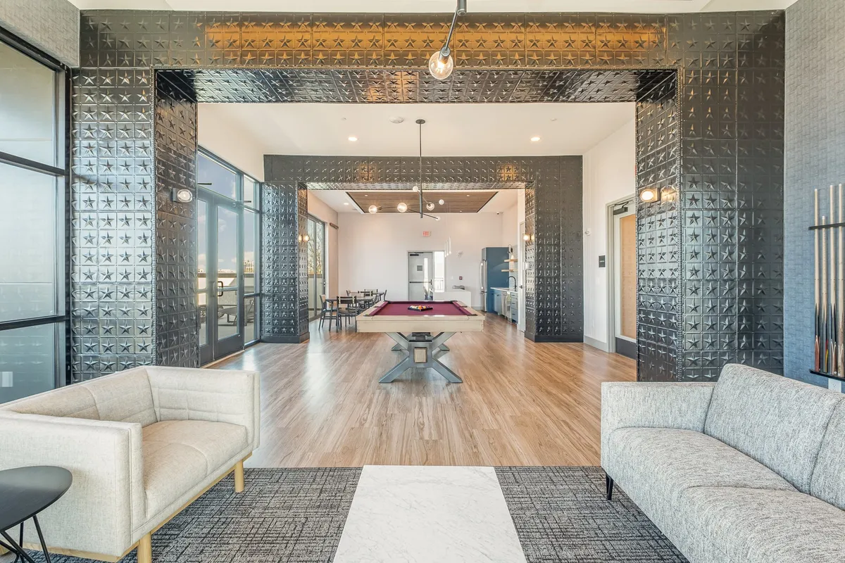 A contemporary lounge space with a pool table at its center, surrounded by modern seating and decorative wall patterns. Large windows provide additional light, creating a friendly and social environment ideal for group activities.