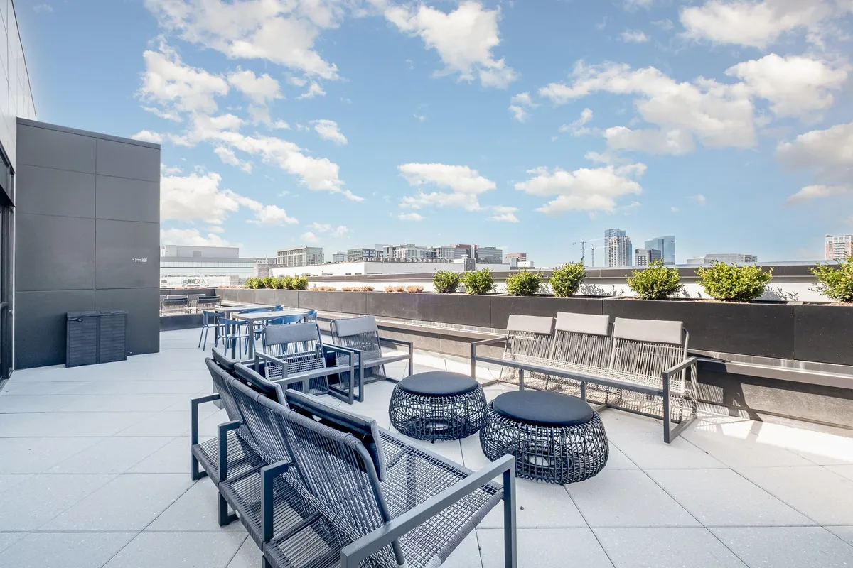 A stylish outdoor seating area with modern furniture, plush cushions, and a panoramic view of the Nashville city skyline. Planter boxes with lush greenery create a welcoming atmosphere for gatherings, relaxation, and enjoying both sunrise and sunset moments.
