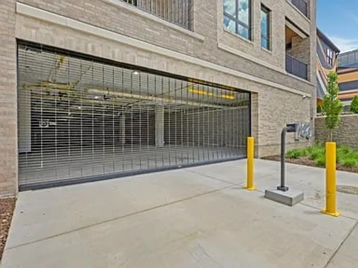 A secure garage entrance with a sturdy security gate, yellow parking poles, and clear signage. The design emphasizes safety and ease of access for vehicles, aligning with the segment's focus on secure garage parking.