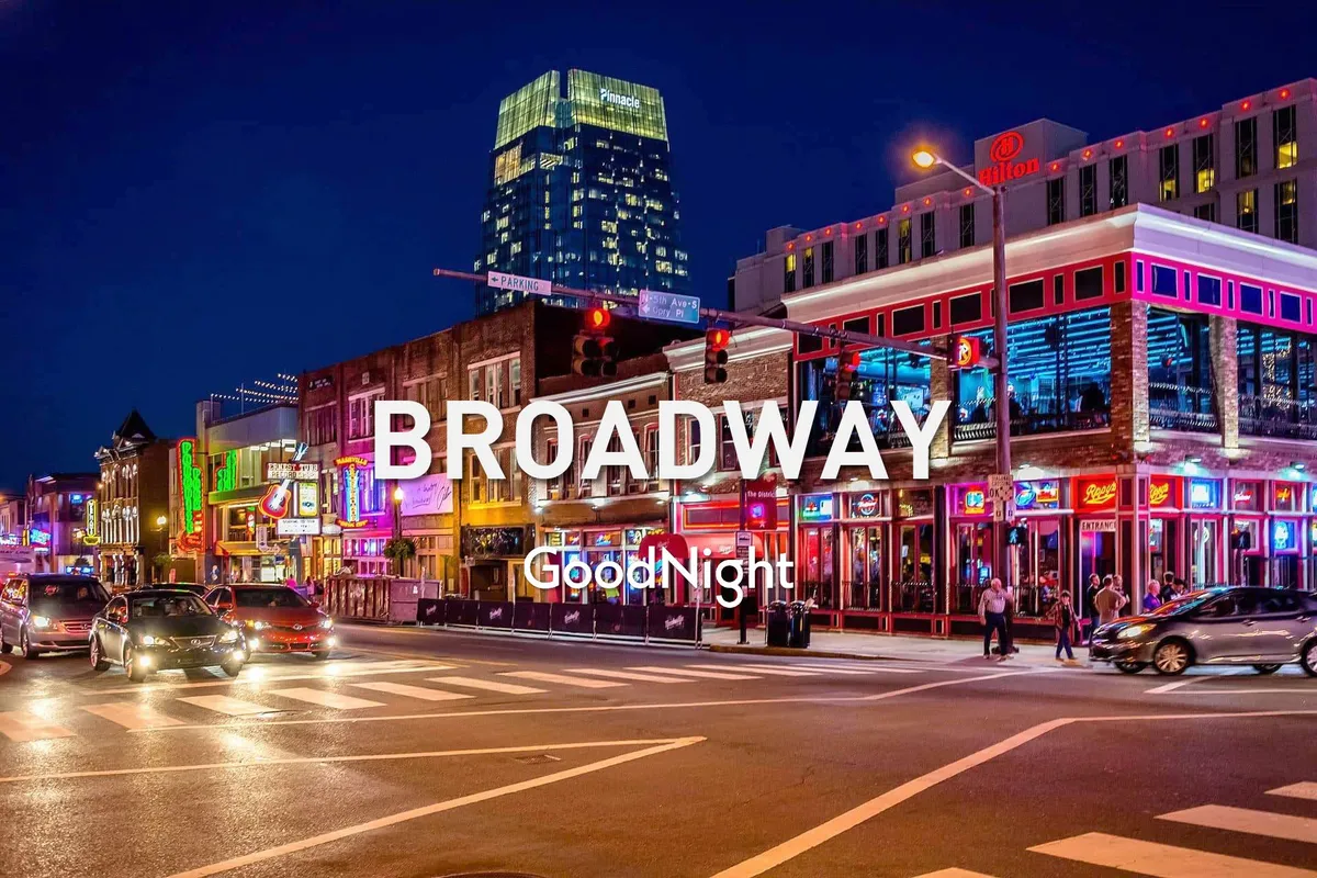 A lively nighttime street scene on Broadway with neon signs, bustling crowds, and the tall buildings of downtown Nashville illuminated in the background. The vibrant energy of the city’s iconic music and nightlife district is unmistakable, with people enjoying food, live performances, and the atmosphere of Music City.