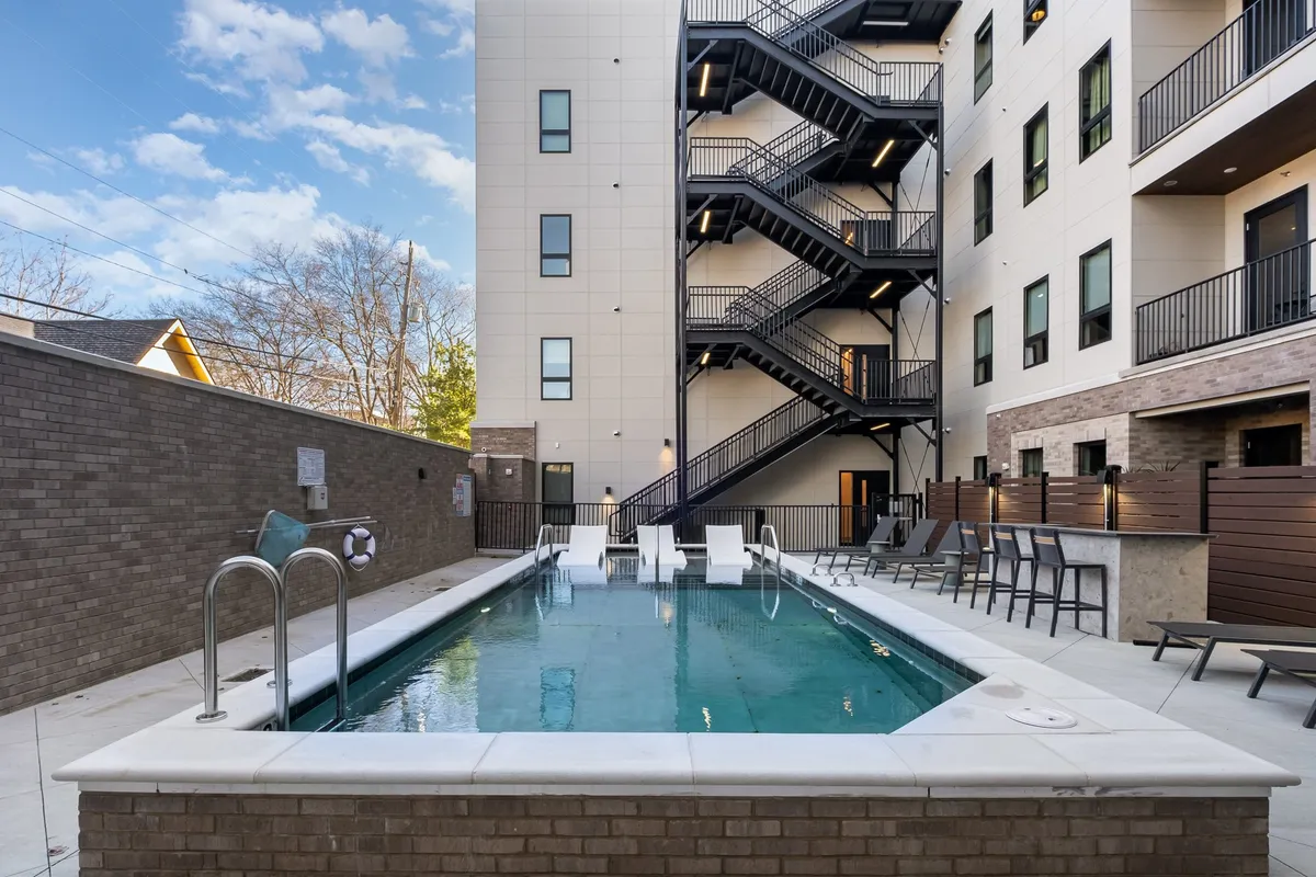 This exterior image features a sparkling swimming pool surrounded by outdoor seating and a staircase, all bathed in natural sunlight. The relaxed atmosphere and inviting setting suggest a perfect spot for families to enjoy afternoons swimming, sunbathing, or socializing during pool season.