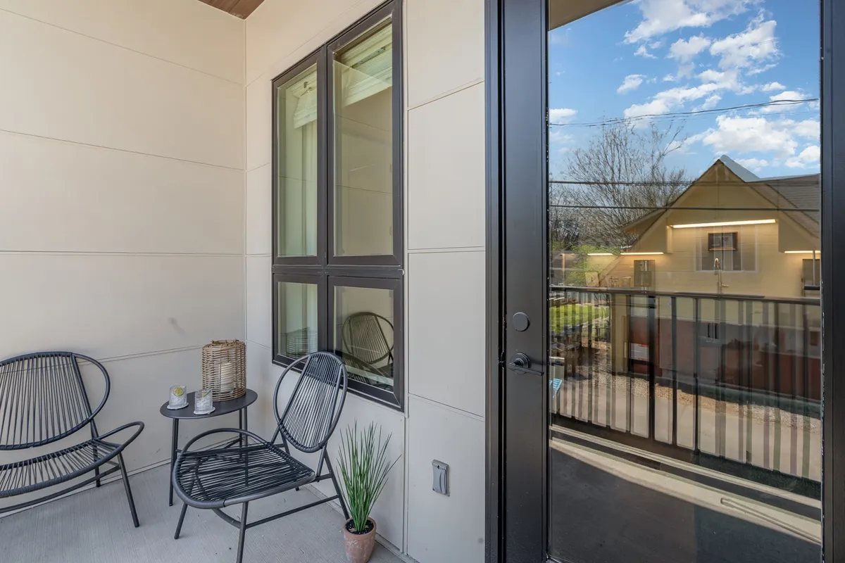 A cozy, private outdoor patio featuring two black chairs, a small table, and a potted plant. The tranquil setting is perfect for enjoying a drink or reading, with sunlight casting gentle shadows across the space.