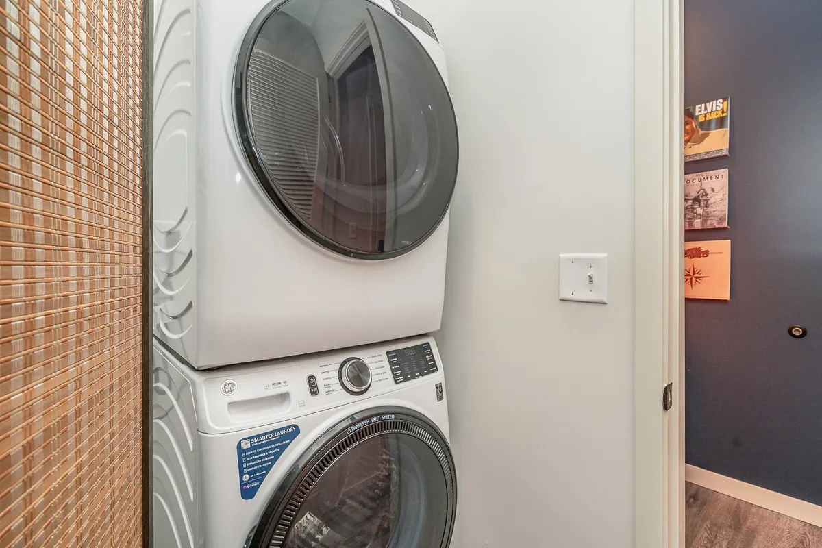 A tidy and efficient laundry area is shown, featuring stacked washer and dryer units, a textured wall, and a doorway leading to another room. The scene communicates the convenience and practicality needed by families traveling with children.